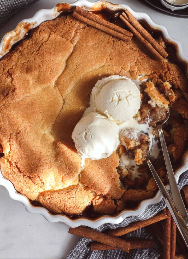 Swedish Apple Pie in a round fluted dish with two scoops of ice cream melting into the pie.