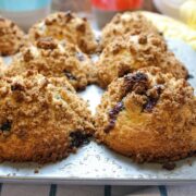 Bakery Style Blueberry Muffins with crumb topping in a muffin tin and a colorful background.