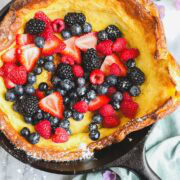 A Dutch Baby in a cast iron skillet loaded with raspberries, blueberries, strawberries, and blackberries and topped wtih powdered sugar.