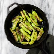 Spanish peppers blistered and sprinkled with flaky sea salt in a black cast iron pan.