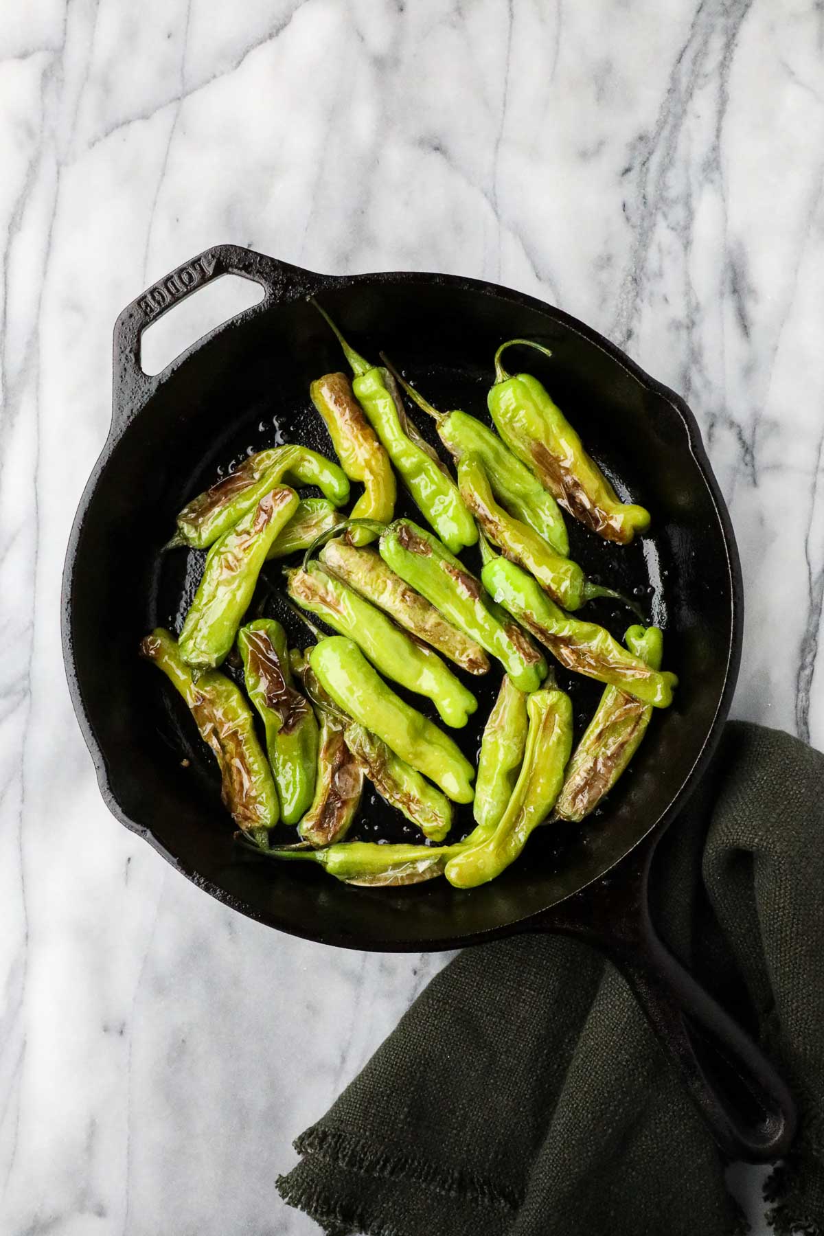 Spanish peppers blistered and sprinkled with flaky sea salt in a black cast iron pan.