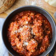 A bowl of Dutch Oven Italian Meatballs on a wooden background with sourdough bread and parmesan.