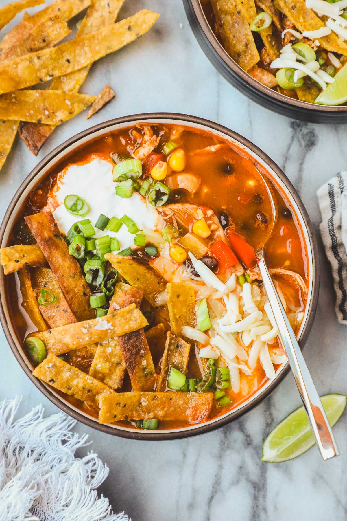 A bowl of Spicy Chicken Tortilla Soup with Monterrey jack cheese, crispy tortilla strips, sour cream, and green onions.