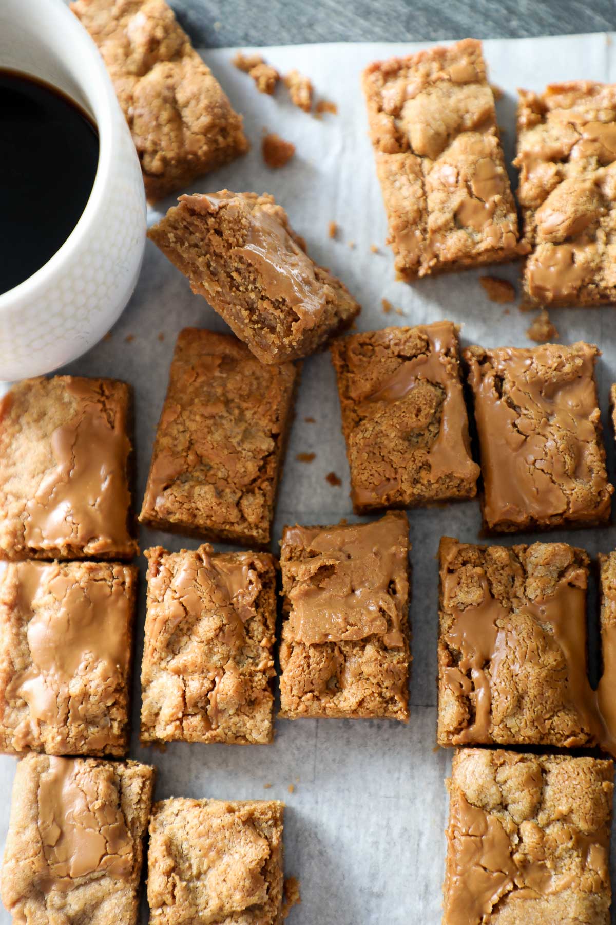 Mini Biscoff Blondies on a light background next to a cup of black coffee in a white mug.