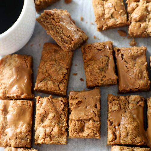 Overhead photo of biscoff blondies cut into small rectangles with a cup of coffee.