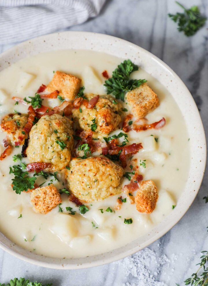 Close up of Creamy Potato Leek Soup with Chicken Meatballs in a bowl with parsley and bacon and croutons on a light background.