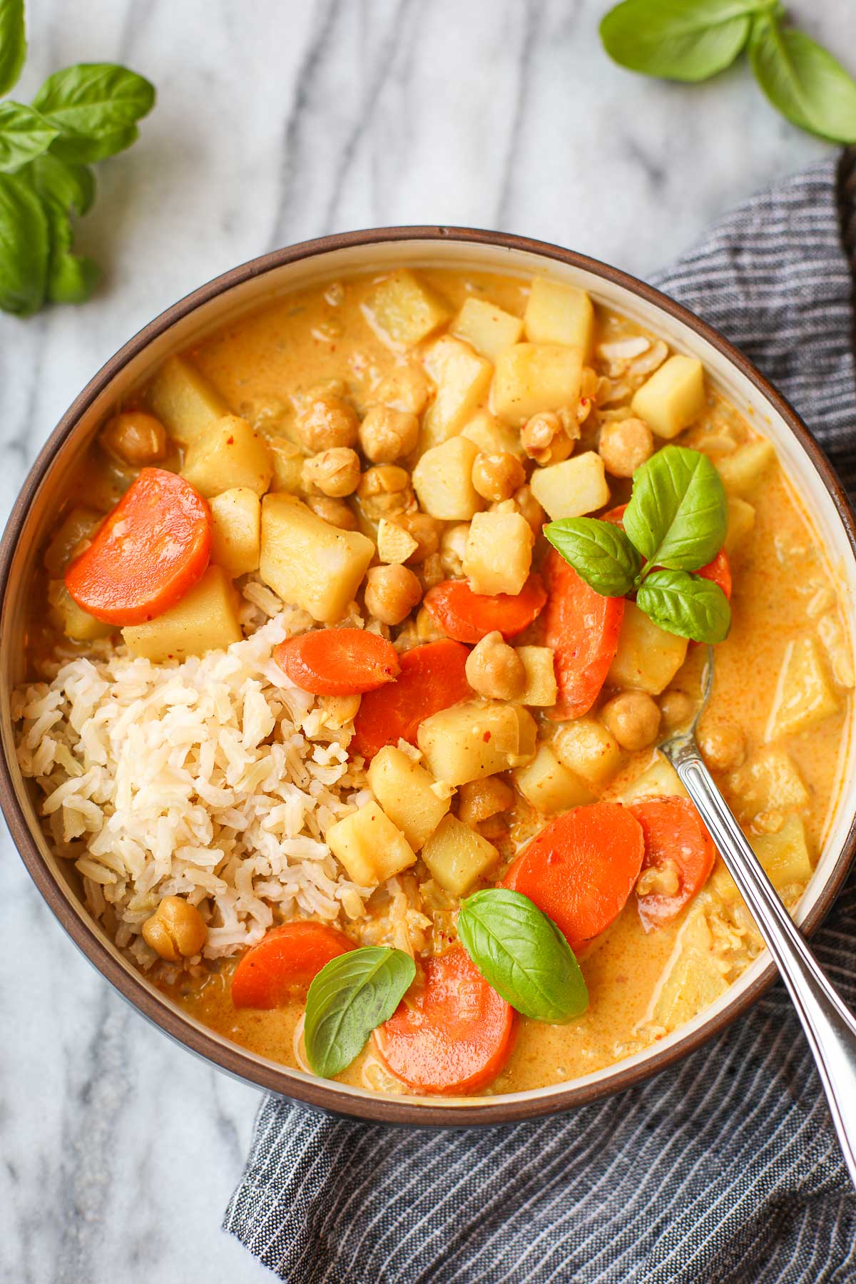 A bowl filled with Yellow Thai Curry with Vegetables with basil for garnish.