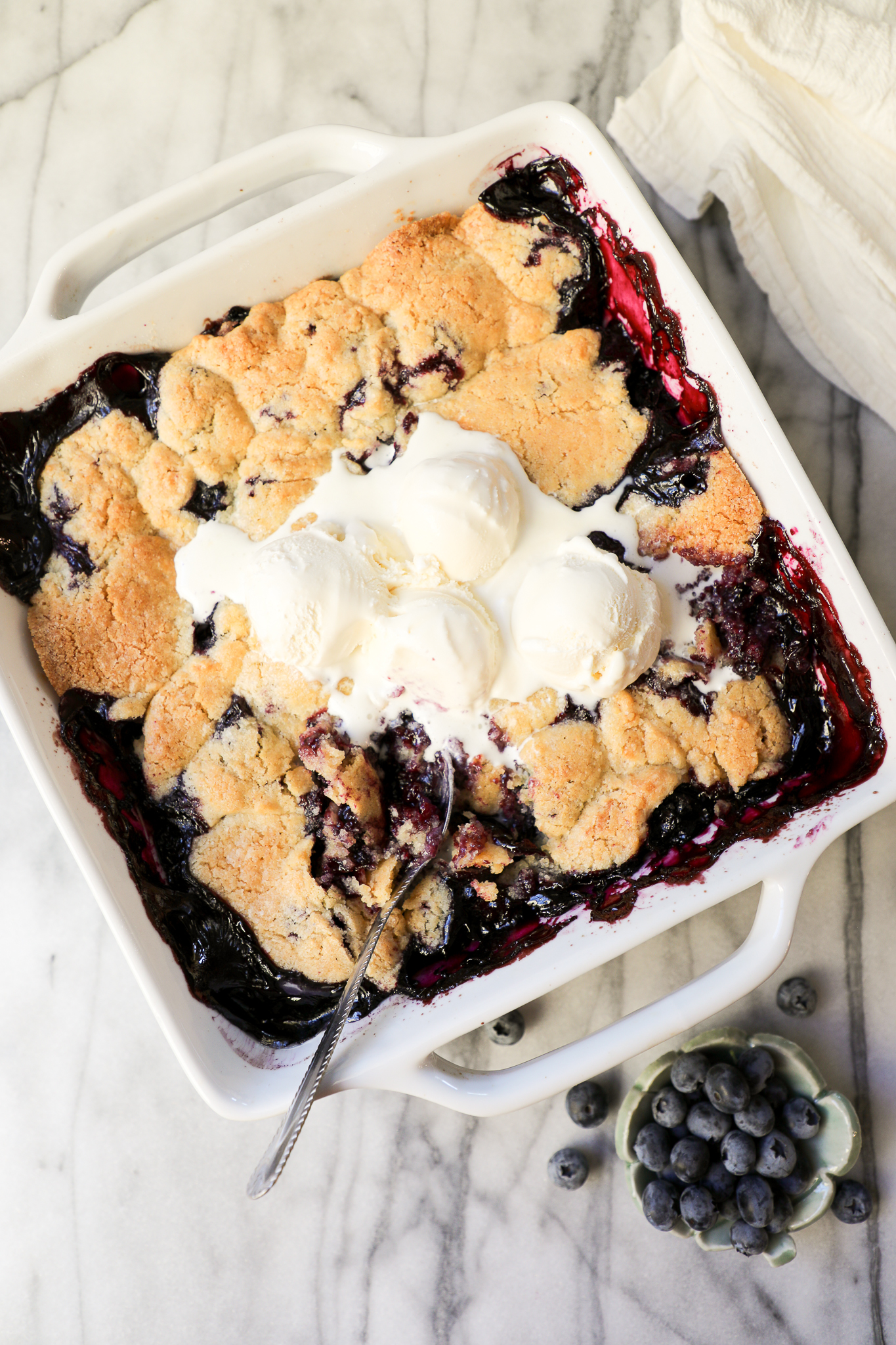 Swedish Blueberry Pie in a square baking dish with melted vanilla ice cream on top.