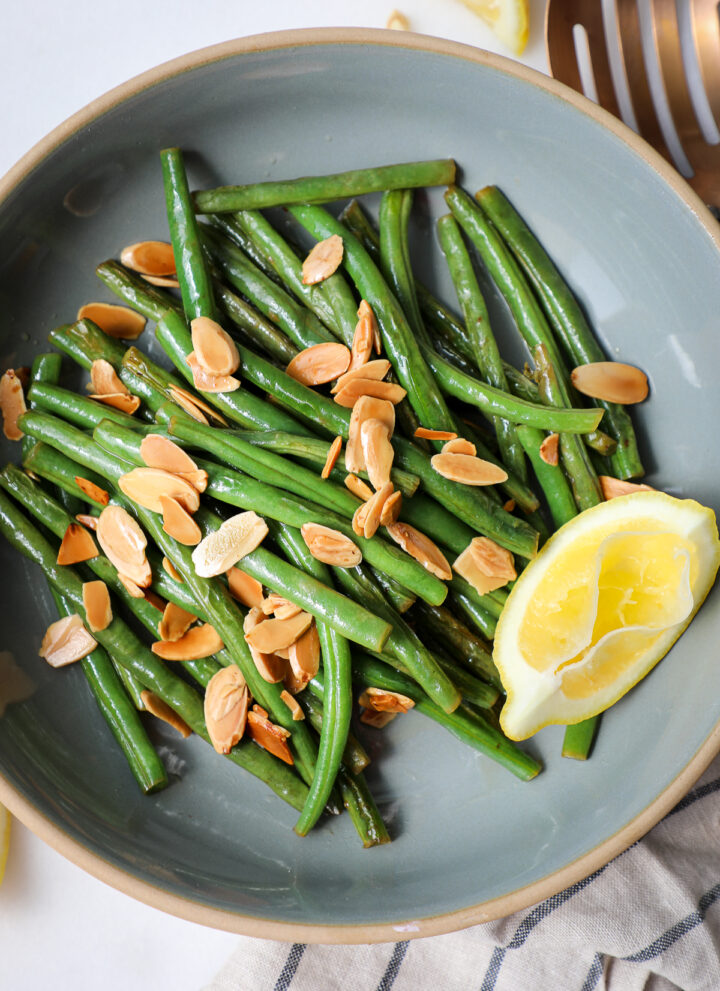 Green beans with toasted slivered almonds in a grey bowl with a squeezed lemon.