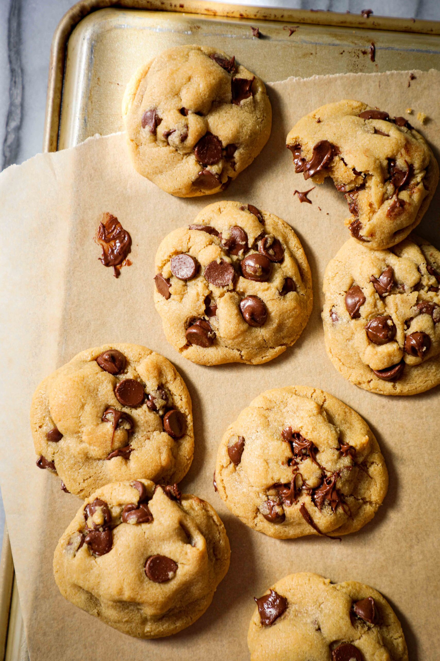 Melty chocolate chip cookies on a gold cookie sheet.