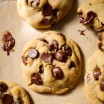 A melty chocolate chip cookie on a gold cookie sheet.