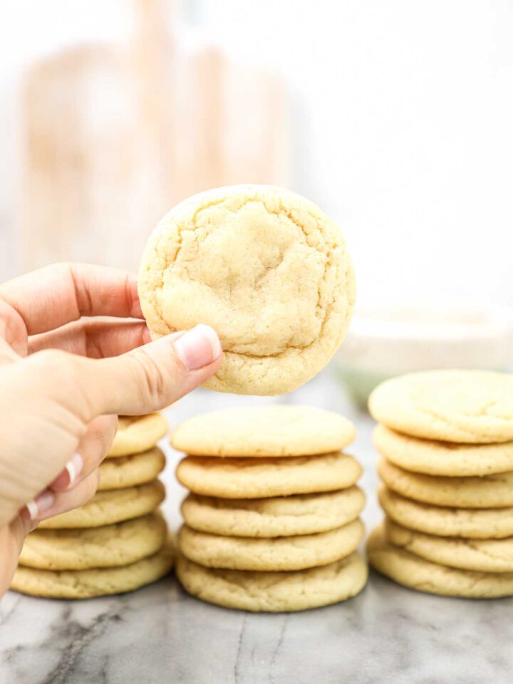 Lauren holding a single sugar cookie with stacks of cookies in the background.