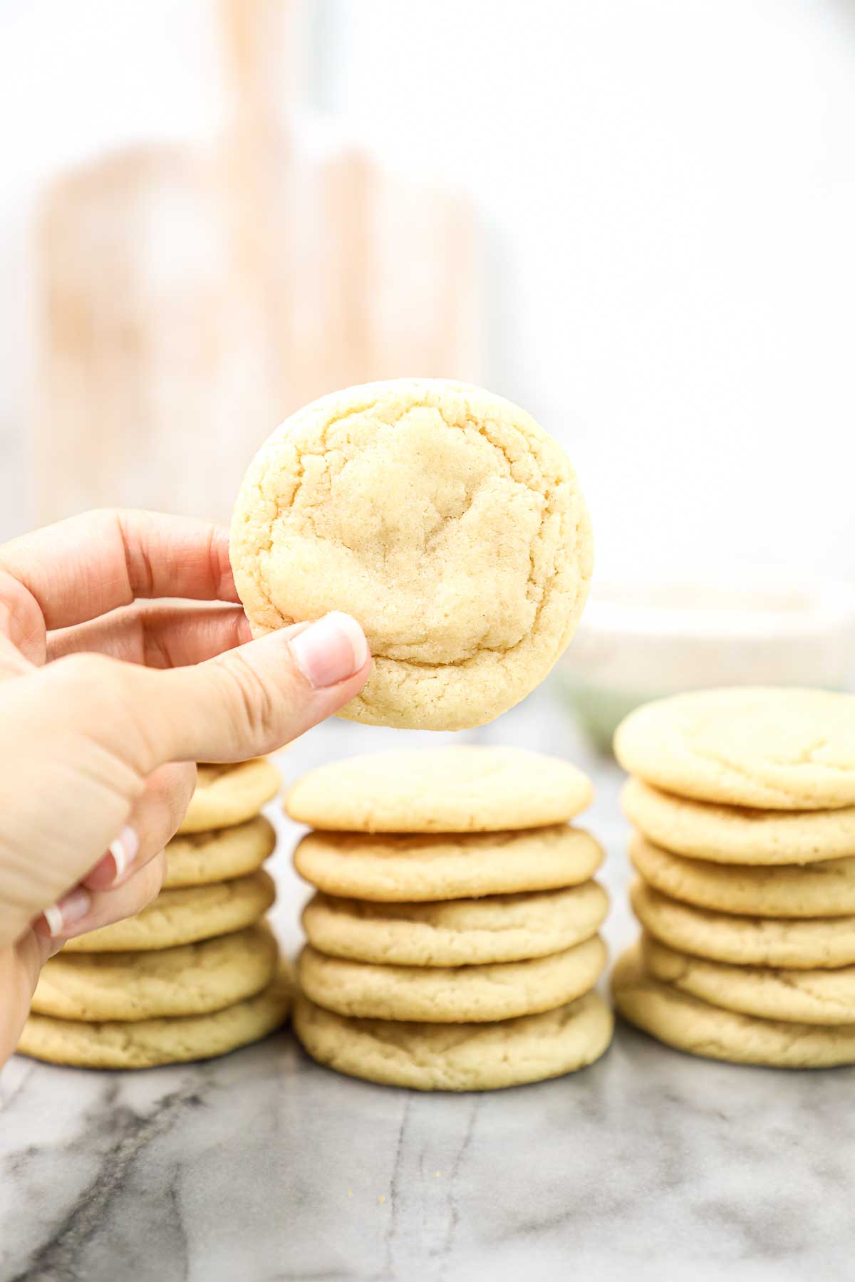 Lauren holding a single sugar cookie with stacks of cookies in the background.