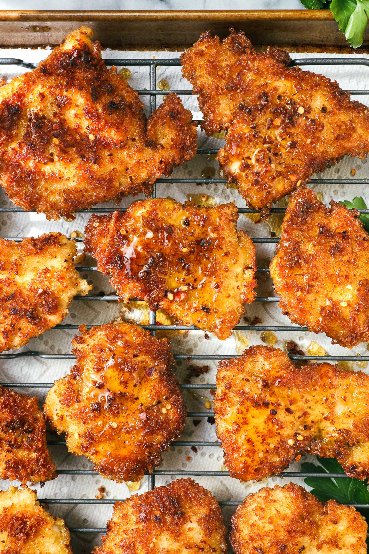 Sheet pan with several pieces of crispy chicken drizzled with hot honey and green beans in the background.