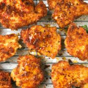 Sheet pan with several pieces of crispy chicken drizzled with hot honey and green beans in the background.