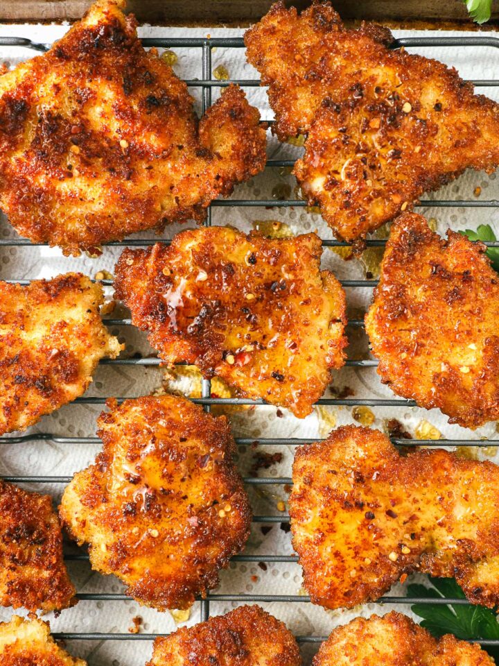Sheet pan with several pieces of crispy chicken drizzled with hot honey and green beans in the background.