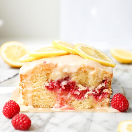 Raspberry Lemon Loaf cross section with lemon glaze dripping over a slice with lemons and raspberries for garnish.