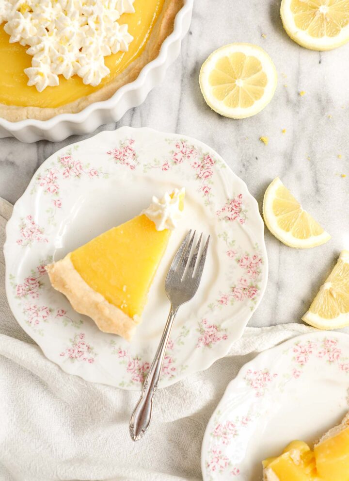 Overhead shot of slices of lemon pie without meringue on white plates with pink flowers and the remaining pie above.
