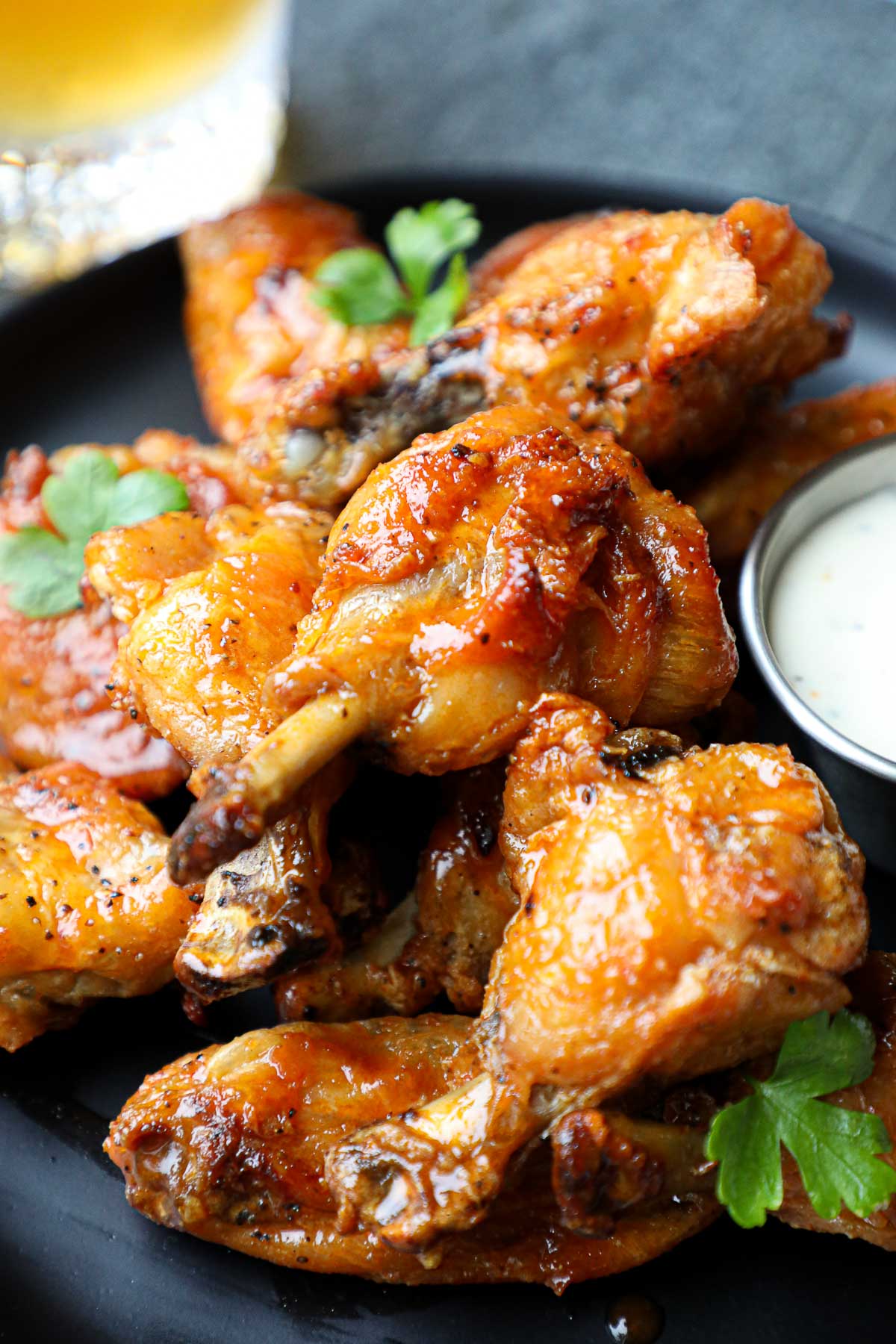 Hoy Honey Lemon Pepper wings stacked on top of each other on a black plate with dipping sauce.