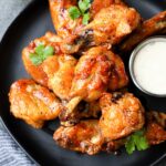 A plate of hot honey lemon pepper wings with ranch dressing dip and a cold beer.