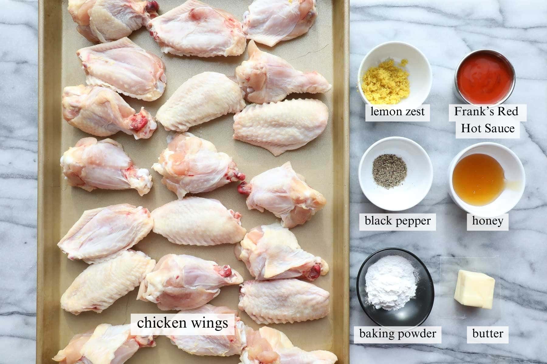 Ingredients for hot honey lemon pepper wings on a marble background.