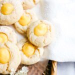 Lemon curd cookies layered on a white cloth over a brown wicker tray with decorative white flowers.