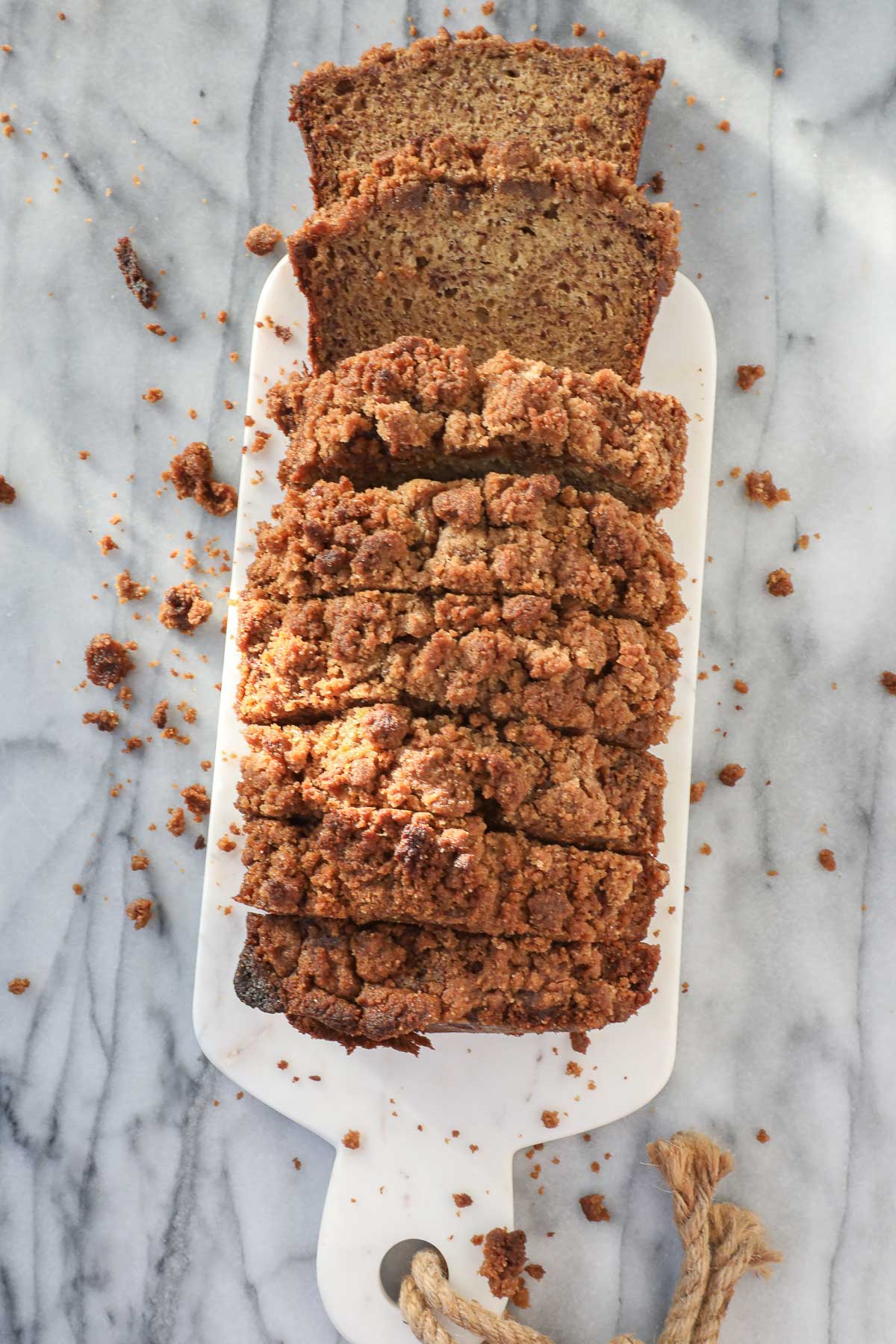 Loaf of banana bread with streusel topping sliced into thick slices on a white serving board.