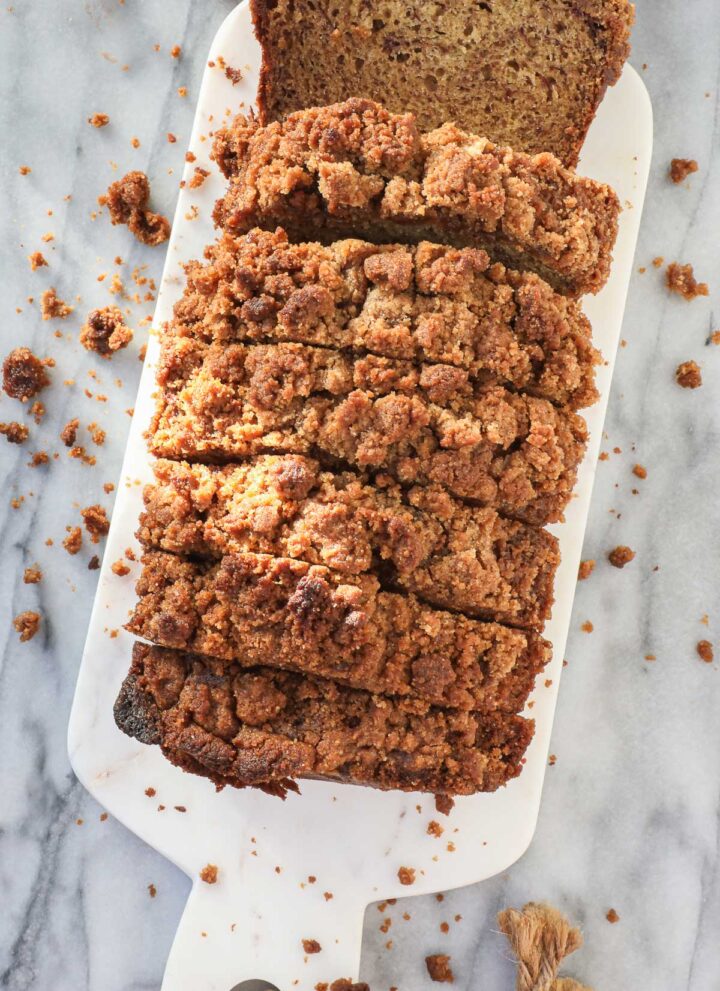 Thick slices of banana bread with streusel topping on a white serving board surrounded by crumbs.