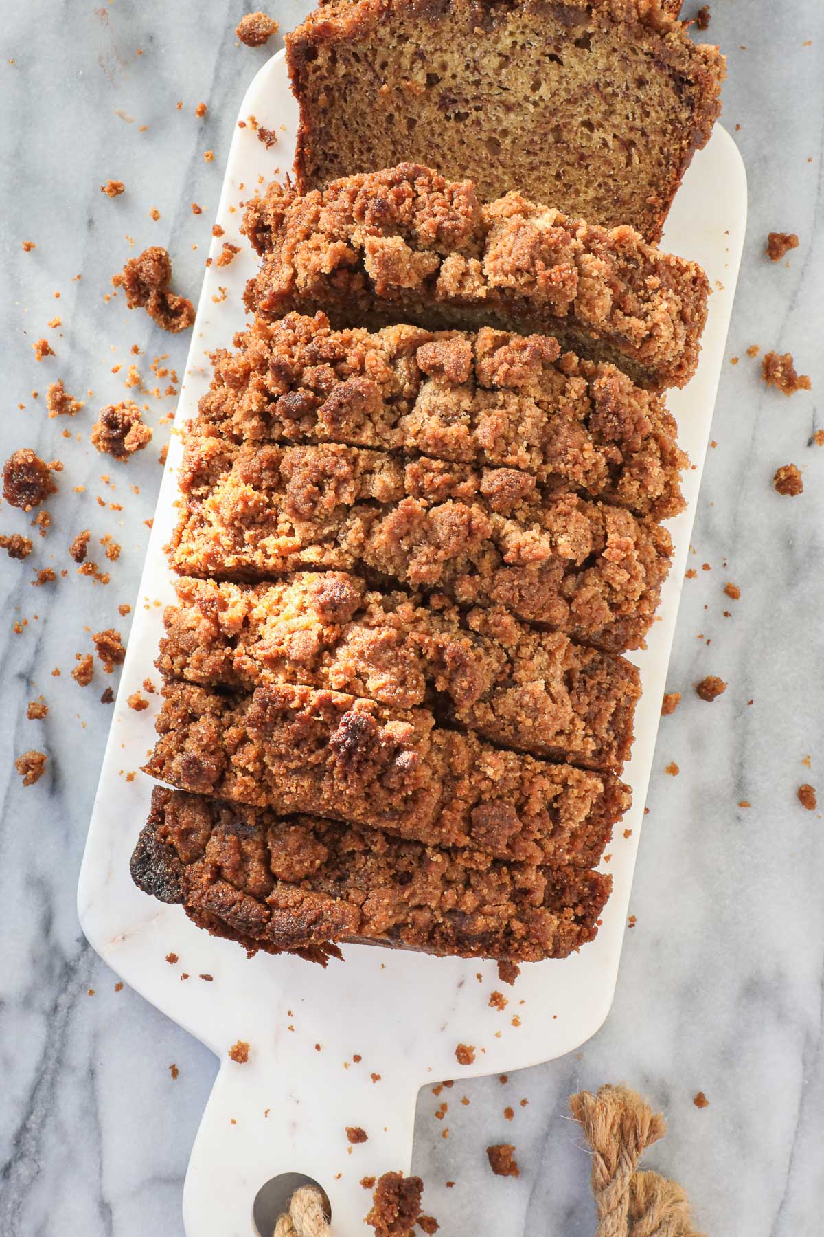 Thick slices of banana bread with streusel topping on a white serving board surrounded by crumbs.