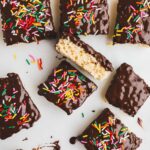 Several Rice Krispie Treats dipped in chocolate and decorated with sprinkles on a white background.