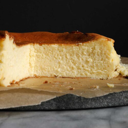 Cross section of cheesecake with a golden brown top, creamy center with a dark background.