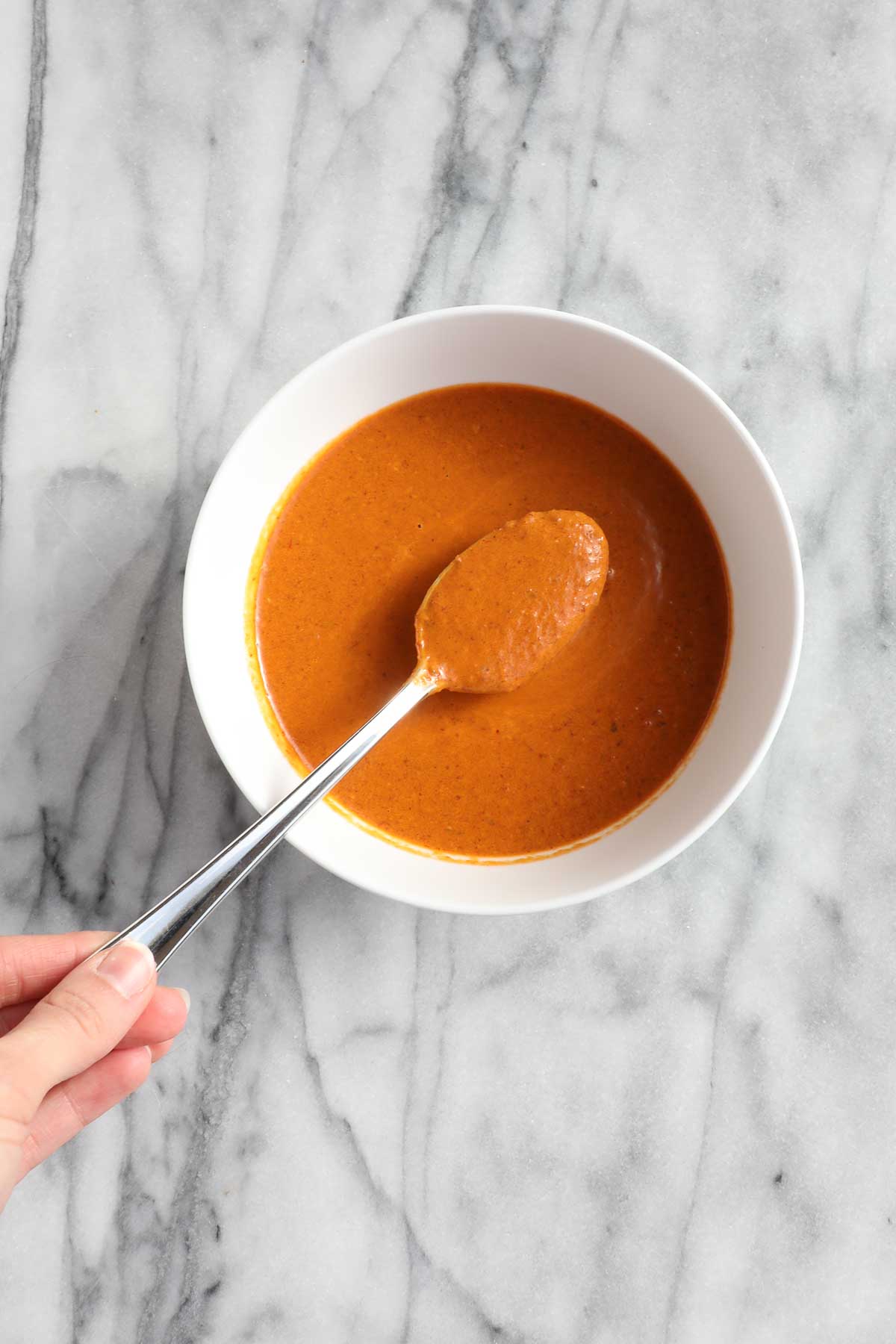 A spoonful of chipotle lime sauce held over a bowl of the sauce.