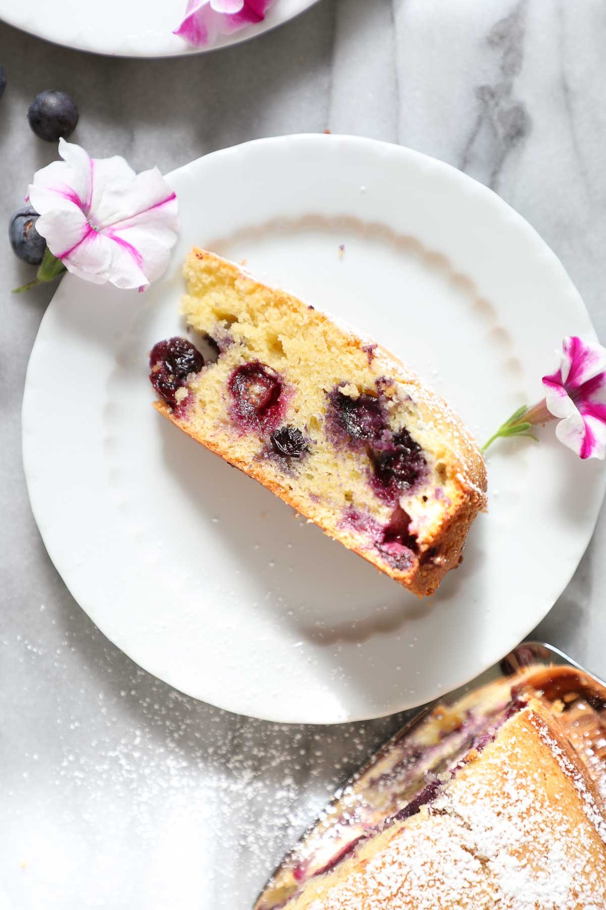 Lemon Blueberry Olive Oil Cake on a small white plate with purple and white decorative flowers.