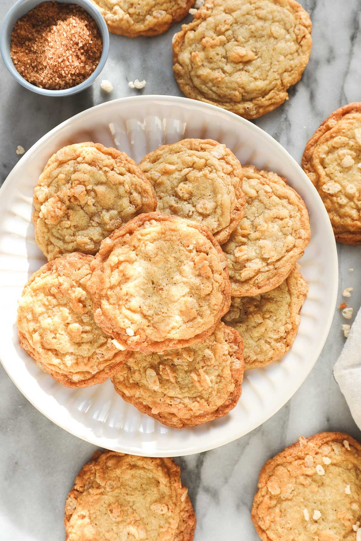 A plate of Crispy Rice Krispie Cookies with dappled sunlight and styled with additional Rice Krispie cookies and a bowl of light brown sugar surrounding the plate.