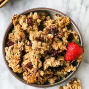 A bowl of Easy Homemade Snacking Granola with lots of large clusters and a few berries on the side.