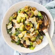 A serving bowl with Hot Honey Brussels Sprouts with Shaved Parmesan and a large gold serving spoon.