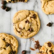 An Einkorn Chocolate Chip Cookie on a white marble backdrop with several cookies including a broken cookie nearby.