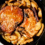 Golden brown bone-in pork chops in a cast iron skillet with baked apples and.