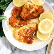 A white plate with 3 crispy chicken cutlets with a lemon sauce.