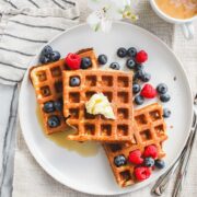 Three Crispy Sourdough Discard Waffles arranged on a white plate topped with butter, maple syrup, blueberries, and strawberries.