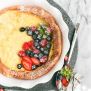A Dutch Baby Pancake in a round fluted ceramic pie dish rather than a cast iron skillet topped with berries and powdered sugar.