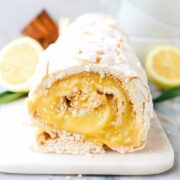 The Meringue Roulade with a cracked white crispy exterior and a lemon filling on a white marble board.
