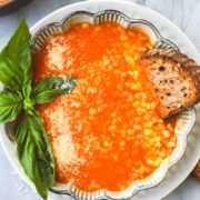 A bowl of Roasted Tomato Garlic Soup with Barley garnished with fresh basil and a slice of toasted bread.