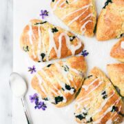 Sourdough Blueberry Scones on a marble board drizzled with lemon glaze decorated with small purple flowers.