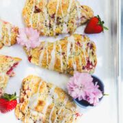 Sourdough Strawberry Scones on a baking sheet with lemon glaze and decorated with strawberries and pink flowers.