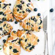 Blueberry Lavender Scones arranged in a circle on a white marble board with lavender petals, fresh blueberries, and white flowers.