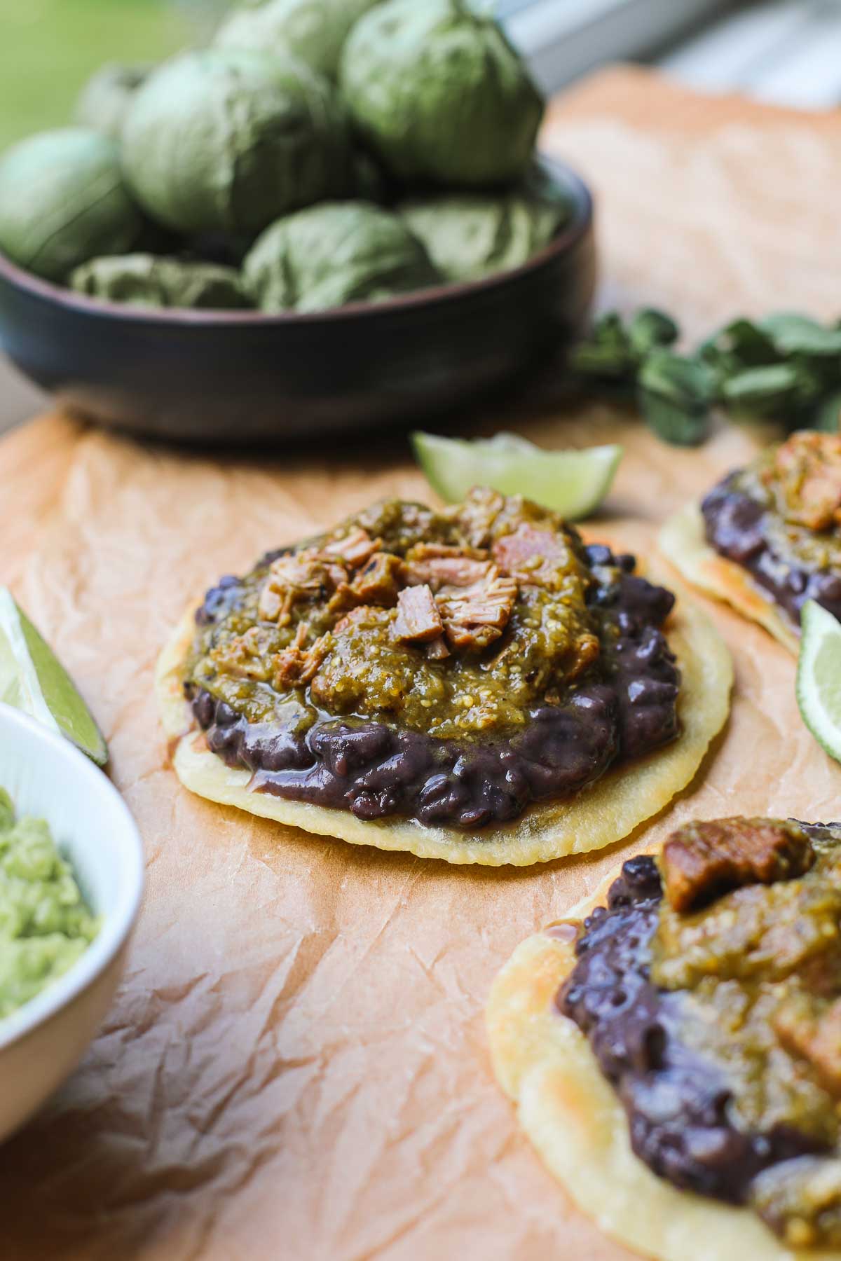 A Green Chili Pork Tostada assembled with the crispy corn tortilla at the bottom layered with refried black beans, and green chili pork.