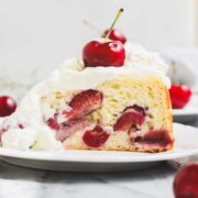 A slice of Ricotta Cherry Cake topped with whipped cream and a single cherry.