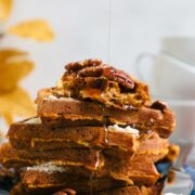 A stack of Sourdough Pumpkin Waffles topped with butter, pecans, and dripping maple syrup.