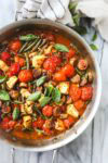 A large sauté pan with baked cherry tomatoes, feta, sausage, and green beans.